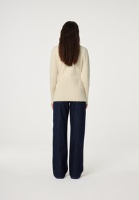 Cream ribbed long-sleeve top paired with wide-leg dark blue denim pants. The top has a fitted silhouette while the pants have a loose fit.