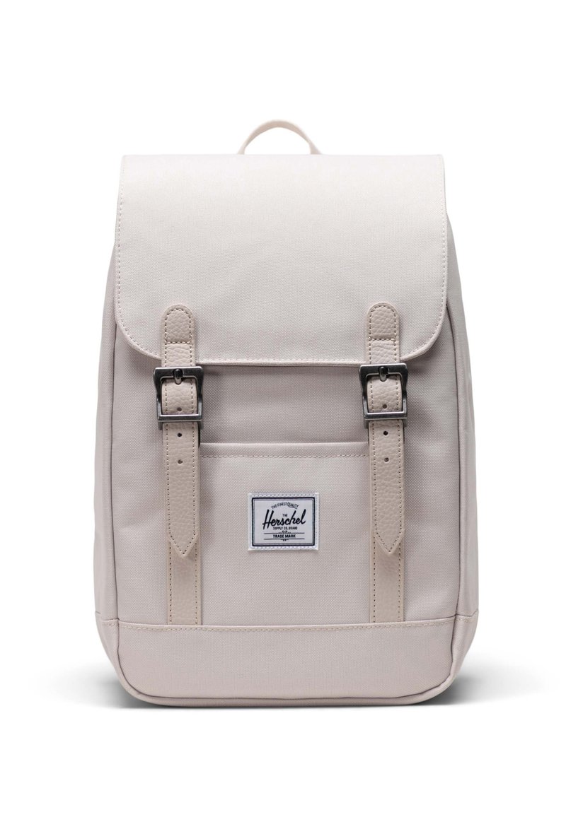 Ljusbeige ryggsäck med lock, två framspännen och en logotypapplikation. Tillverkad av slitstarkt tyg, med rektangulär form och slät textur.