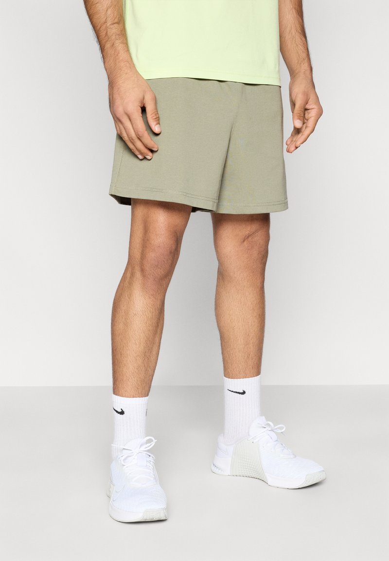 Χακί σορτς με άνετη εφαρμογή, κατασκευασμένα από βαμβάκι με λεπτές ραφές, συνδυασμένα με λευκά αθλητικά παπούτσια και κάλτσες με λογότυπο.