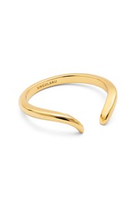 Pulsera de brazo de metal dorado con acabado suave y pulido. Presenta un diseño abierto con extremos afilados y un sutil logotipo en el interior.