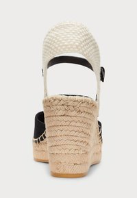 Černé espadrilové wedge s pletenou jutu patou, s tkaným bílým svrškem a nastavitelným zápěstním páskem. Texturovaný povrch a pevná základna.