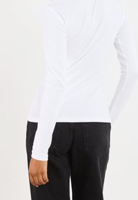 Pitkähihainen valkoinen ribbineulospaita, jossa on istuva siluetti ja pyöreä pääntie, yhdistetty tummansinisiin korkeavyötäröisiin farkkuihin.