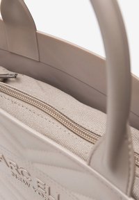 Borsa tote di un beige chiaro con un esterno testurizzato, caratterizzata da un design cucito e un'apertura superiore che rivela un interno di colore crema con chiusura a zip.