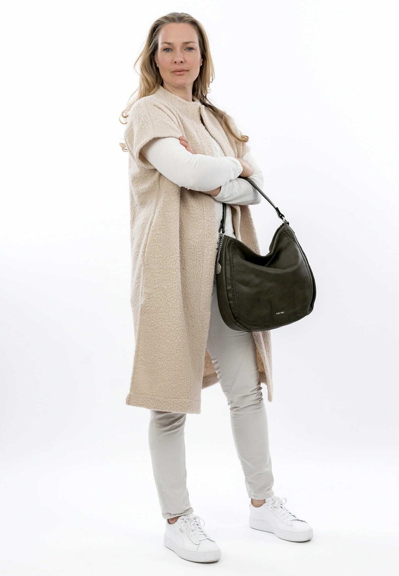 Beige fleece overtøj med korte ærmer, lysegrå bukser og hvide sneakers. Bærer en mørkegrøn læder skuldertaske.