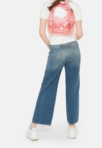 Transparent rosa ryggsäck med justerbara remmar och två fickor med dragkedja, kombinerat med lösa blå jeans och vita sneakers.