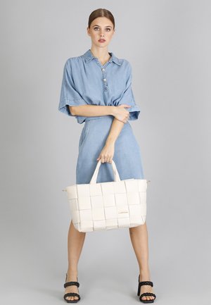 Witte geweven tote bag met dubbele handvatten, rechthoekige vorm, gladde textuur en gouden hardware details. G gedragen met een denim shirtjurk.