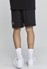 Black athletic shorts with a relaxed fit, featuring an embroidered "PALK" detail. Paired with white Nike Air sneakers and crew-length socks.