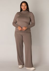 Bruine, lange mouwen turtleneck top gecombineerd met bijpassende wijde broek, beide gemaakt van zacht, rekbaar materiaal. Schoeisel: lichtgekleurde sneakers.