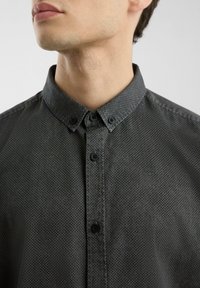 Camisa de botones de color gris oscuro con un patrón texturizado, que presenta un cuello estándar y botones negros en la parte delantera.