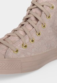 Κοντινό πλάνο σε ανοιχτό ροζ ψηλό sneaker με υφασμένο λουλουδάτο σχέδιο, μπεζ κορδόνια και χρυσά μεταλλικά οπές.