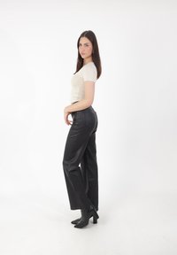 Camiseta ajustada beige, pantalones de imitación de cuero negro de cintura alta y botines de tacón negro, todo sobre un fondo blanco.