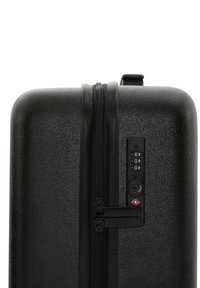 Hård-skal svart resväska med texturerad yta, dubbel svart dragkedja och en kombinationslåspanel med TSA-logotyp på sidan.