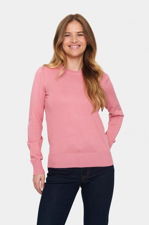 Rózsaszín kötött pulóver hosszú ujjal, kerek nyakkivágással és bordázott szegéllyel. Simább textúrájú, finom függőleges csíkokkal. Sötét farmernadrággal párosítva.