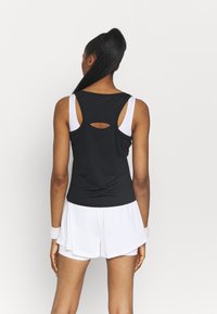 Top deportivo negro sin mangas con un escote en la espalda, combinado con pantalones cortos blancos. El top cuenta con tirantes anchos y una textura lisa.