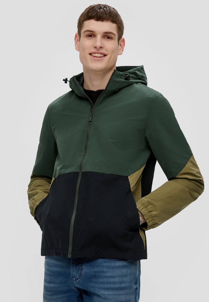 Gevoerde jas met een groene bovenkant, olijfgroene en zwarte onderdelen. Heeft een rits, elastische manchetten en zijzakken. Gladde textuur.