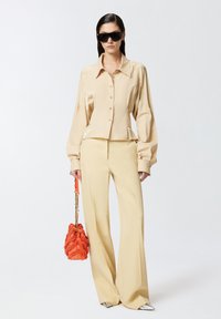 Bež košulja s dugim rukavima i napuhanim rukavima, u kombinaciji s bež hlačama širokih nogavica. Upotpunjena je teksturiranom narančastom torbom i metalik cipelama.