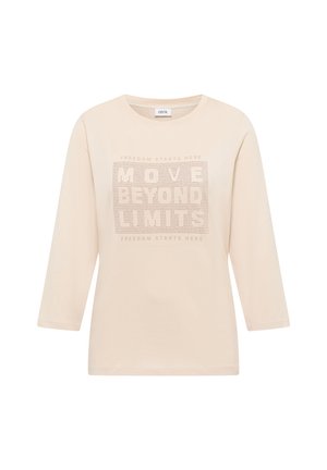 Jersey beige con mangas tres cuartos, con un diseño gráfico texturizado que incluye el texto "MOVE BEYOND LIMITS" y pequeños agujeros.