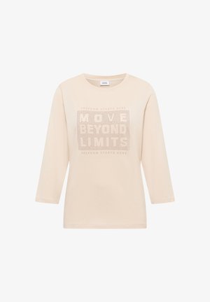 Jersey beige con mangas tres cuartos, con un diseño gráfico texturizado que incluye el texto "MOVE BEYOND LIMITS" y pequeños agujeros.