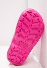 Semelle en caoutchouc rose d'une chaussure Crocs, présentant un motif de semelle avec des textures rectangulaires et circulaires et un logo en relief.