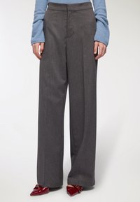 Szare damskie spodnie z wysokim stanem i szerokimi nogawkami, wykonane z fakturowanej tkaniny, cechujące się czystymi liniami i dopasowanym krojem, zestawione z czerwonymi, spiczastymi butami.