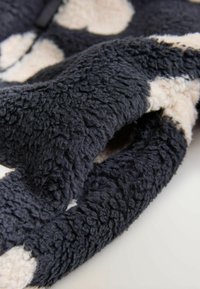 Blødt sort og hvidt fleece-stof med en tekstureret, fluffy overflade og en delvist foldet sektion.