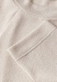 Crème-kleurige gebreide trui met een geribbelde textuur, brede halslijn en omgeslagen mouwdetails. Zacht materiaal met een losse pasvorm.