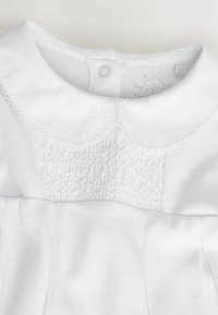 Witte jurk met een afgeronde kraag, voorzien van plooien en een gerimpeld ontwerp op het lijfje. Zacht katoenen materiaal voor comfort en duurzaamheid.