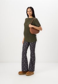 Pull à col rond en tricot vert olive avec un motif texturé, associé à un pantalon évasé noir avec un imprimé floral blanc et un sac à main marron.