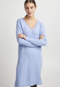 Vestito maglione a V in azzurro chiaro, in tessuto lavorato a maglia con una consistenza morbida. Maniche lunghe e vestibilità leggermente oversize, rifinito con polsini a costine.