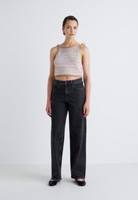 Stribet, cropped strik tanktop med båndremme parret med højvædede, mørkegrå vidde jeans. Flade sorte sko fuldender outfittet.