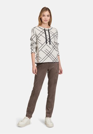 Haut à manches longues gris clair avec des lignes géométriques noires et un design de pull à col en V, associé à un pantalon en suède brun et des baskets blanches.