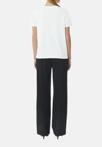 Witte T-shirt met korte mouwen en een ronde hals, gecombineerd met zwarte wijde pijpen. De stof lijkt glad en casual.