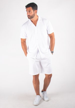 Chemise blanche à manches courtes et shorts assortis en tissu léger. Dotée d'un col, d'une fermeture à boutons et de baskets blanches sportives.