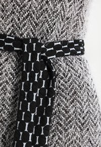 Tessuto grigio e nero con una trama texturizzata caratterizzato da un intreccio soffice, con una cintura nera a contrasto decorata con forme ovali e accenti azzurri chiari.