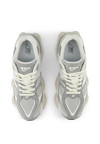 Parica sivih in belih superg New Balance 9060 za tek, z mrežastimi in semiš gornji deli, kremnimi vezalkami in masivnimi bež podplati, vidno od zgoraj.