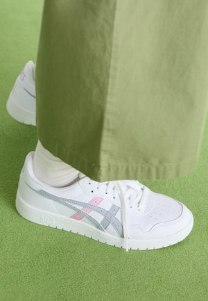 Bele tenisice z izvedbo v sivi in rožnati barvi, z gladkim usnjenim zgornjim delom, perforiranim prednjim delom in ravnim belim podplatom, v kombinaciji z olivno zelenimi hlačami.