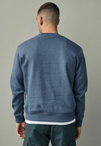 Sweater bleumarin cu manșete și tiv din tricot, fabricat dintr-un material moale. Are un guler clasic tip crew și o croială lejeră.