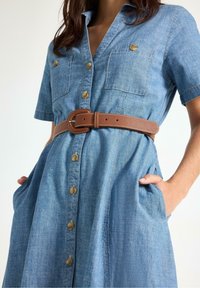 Jeansklänning med korta ärmar, knäppning framtill, två bröstfickor och ett brunt bälte. Lättviktig tyg med en mjuk textur.