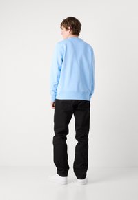 Maglione azzurro chiaro con polsini a coste, abbinato a pantaloni neri e sneakers bianche. Il tessuto appare morbido con un design a vestibilità rilassata.