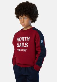 Felpa rossa con maniche blu navy, testo frontale "NORTH SAILS 1957" in bianco, colletto e polsini a coste, con un patch del logo sulla manica.
