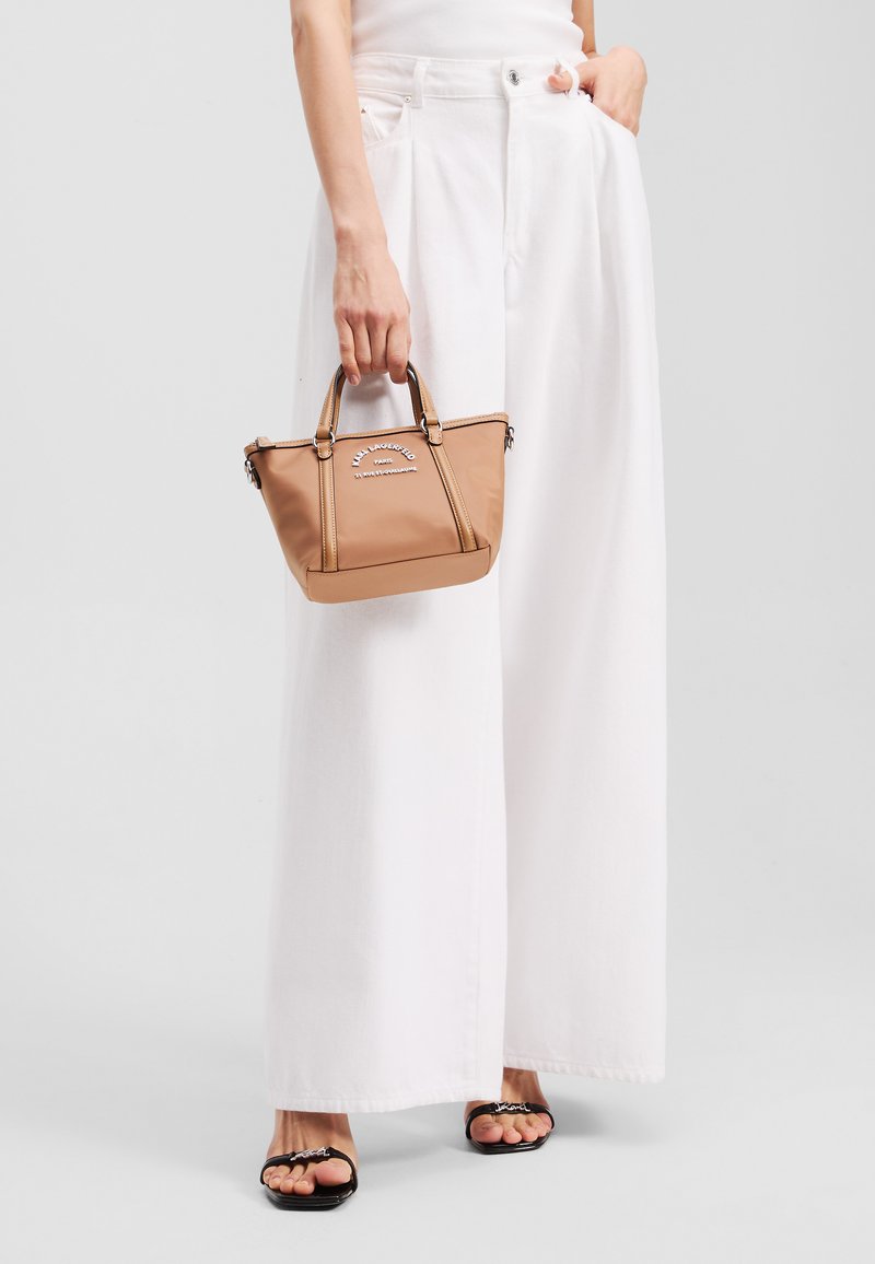 Tan handbag with a structured design, zipper closure, and dual short handles. Accented with logo print and contrasting stitching.