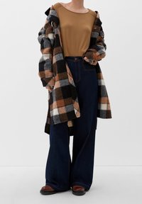 Sweter w kratę z wełny w kolorze czarnym, brązowym i szarym; brązowa bluzka z długim rękawem; ciemnoniebieskie dżinsy o szerokich nogawkach; brązowe buty z teksturowaną podeszwą.