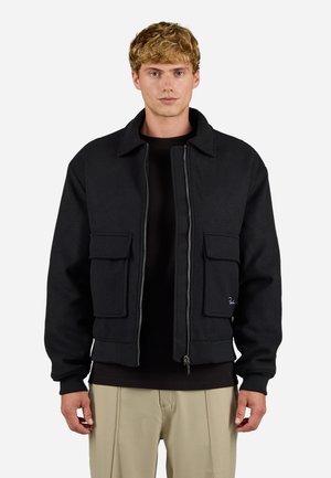 Black bomber jacket made of textured fabric, featuring a zip front, two large front pockets, and ribbed cuffs. Simple, functional design.