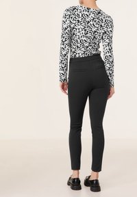 Svarta slim-fit byxor med en slät textur och bakfickor, tillsammans med en vit och svart abstrakt mönstrad figurnära långärmad topp.