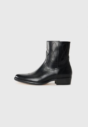 Black leather ankle boot with a pointed toe, decorative stitching, and a low block heel. Smooth texture with subtle design accents.