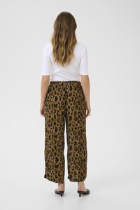 Pantalons à jambes larges en imprimé léopard dans un tissu brun et noir, avec une taille élastique confortable, associés à un haut blanc ajusté.