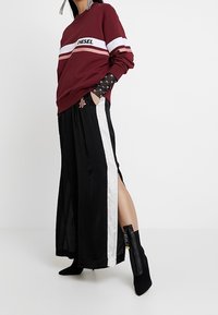 Felpa bordeaux con strisce bianche e rosse, con il logo "DIESEL". Abbinata a pantaloni larghi neri con una striscia laterale bianca e stivali con zip.