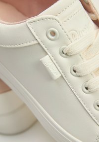 Białe syntetyczne sneakersy o teksturowanej powierzchni, z kremowymi sznurówkami, metalowymi oczkami i małą białą metką z logo po boku.