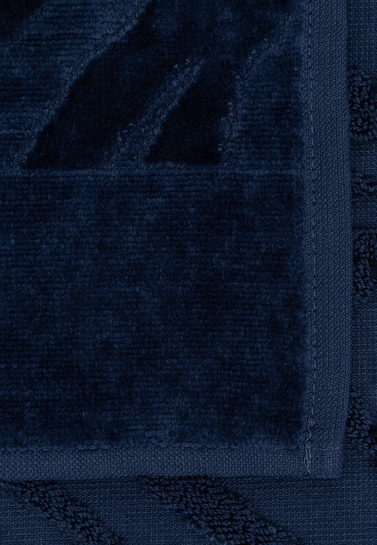 Toalla de color azul marino con una superficie de felpa texturizada y un patrón geométrico en contraste. Bordes acabados con textura en bucle. Tela suave y absorbente.