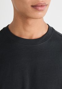 Schwarzes Baumwoll-T-Shirt mit Rundhalsausschnitt. Verfügt über eine glatte Textur und dezente Nähedetails am Kragen und an den Schultern.